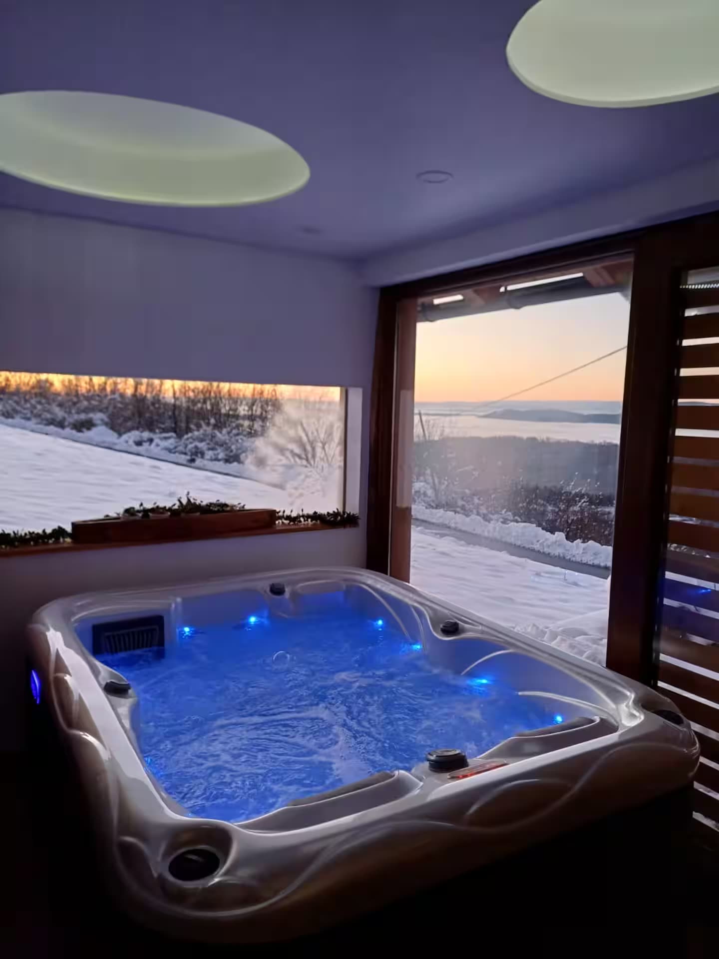 Unutarnji jacuzzi uz panoramski prozor s pogledom na snijeg i zalazak sunca